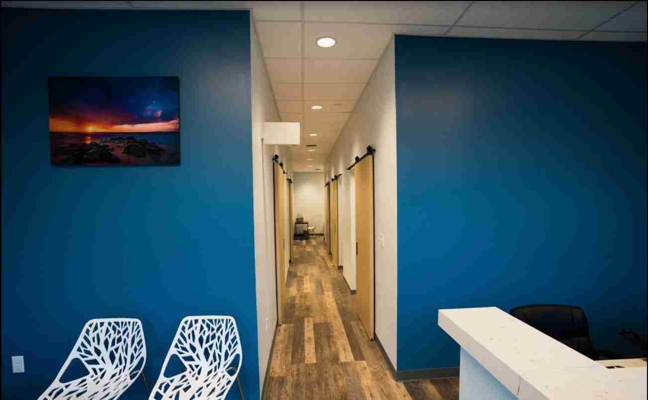 The waiting area of Dr. Paul Morton's Honolulu orthopedic clinic with blue walls, modern white chairs, and a hallway to exam rooms.