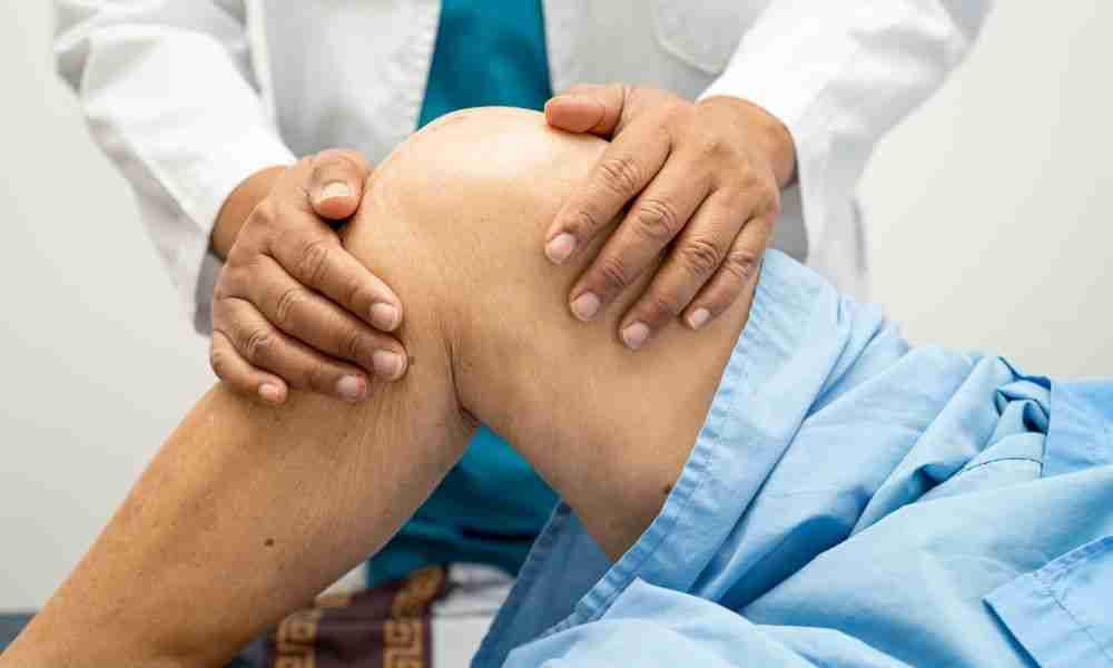 A physician examines a patient's knee during an evaluation for post-traumatic arthritis.