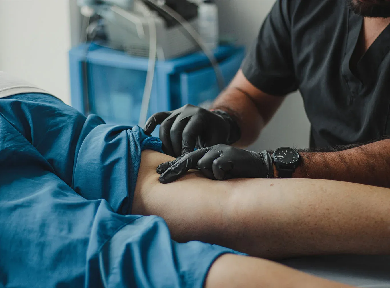 Clinician in black gloves preparing a patient's leg for an injection procedure.