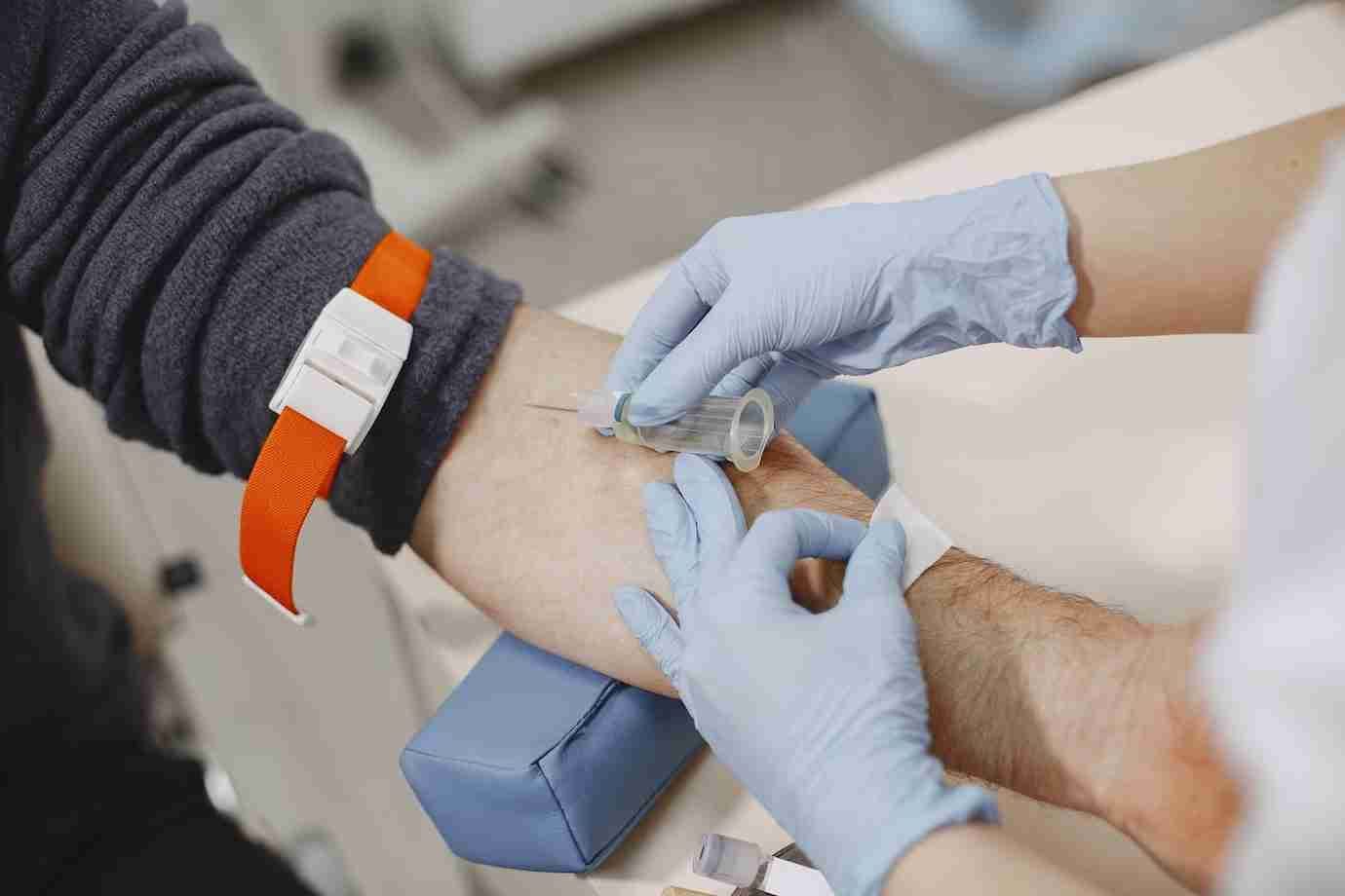 A gloved clinician draws a blood sample from a patient's arm.
