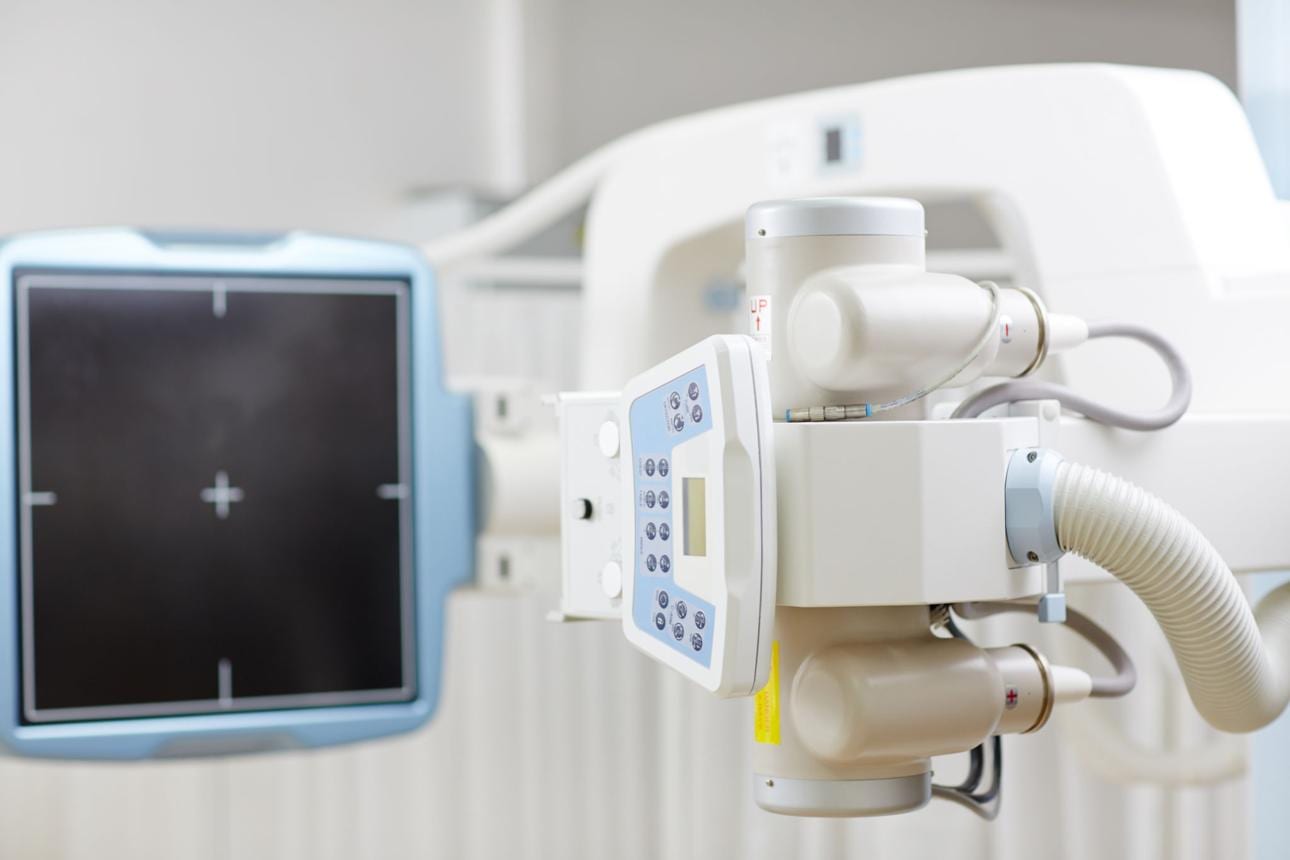 A digital X-ray machine and detector panel in a clinic imaging room — on-site X-ray means injuries are diagnosed on the spot.