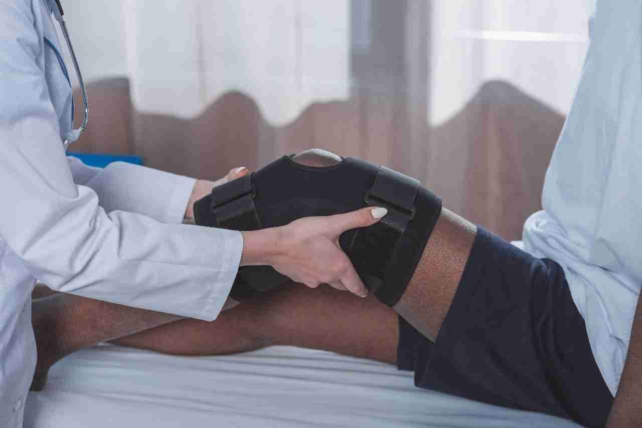 A doctor fits a supportive knee brace on a patient's leg during an exam.