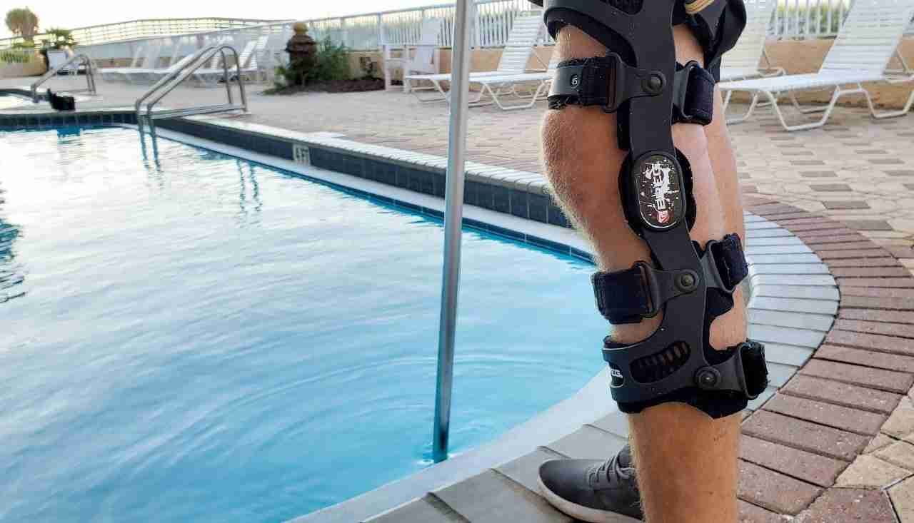 A man wearing a hinged functional knee brace stands beside a swimming pool.