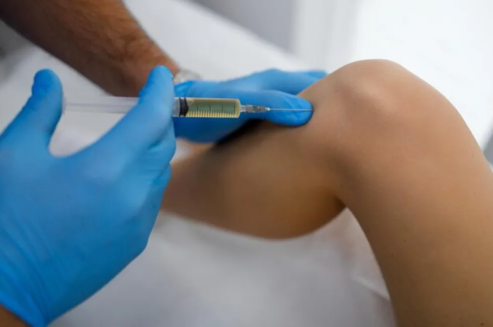 A gloved clinician injects medication into a patient's knee joint, as done for hyaluronic acid gel injections.
