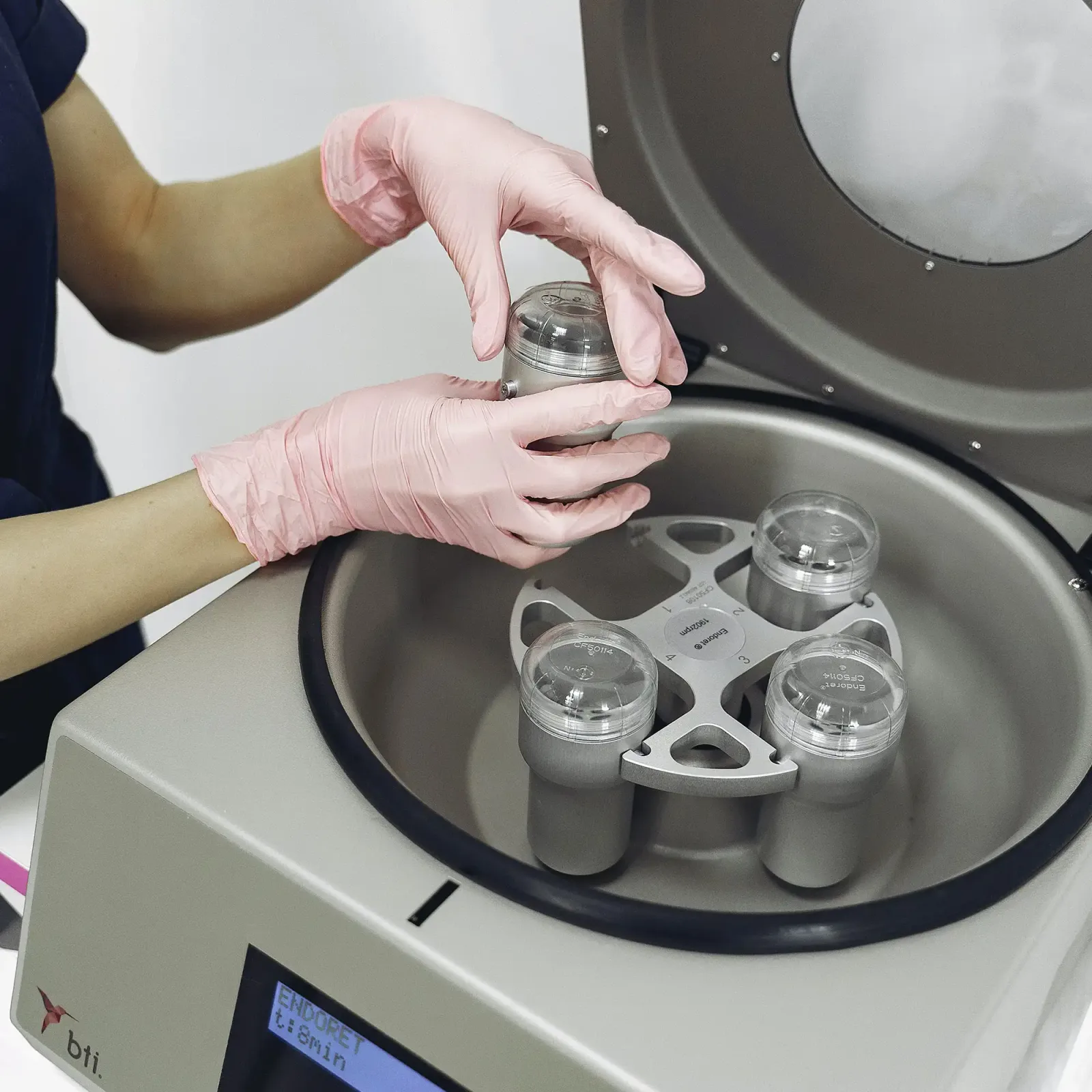 Gloved technician loading blood collection tubes into a centrifuge used to prepare platelet-rich plasma.