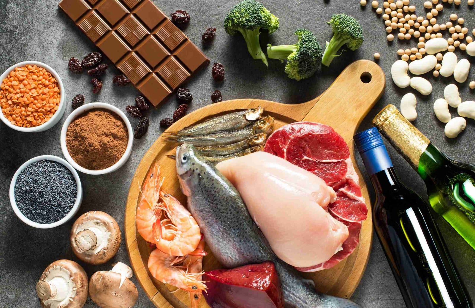 Fish, chicken, lean beef, broccoli, beans, and dark chocolate arranged on a cutting board — protein-rich foods that support healing after surgery.