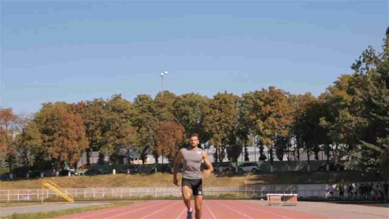 A male athlete runs on an outdoor track on a sunny day.