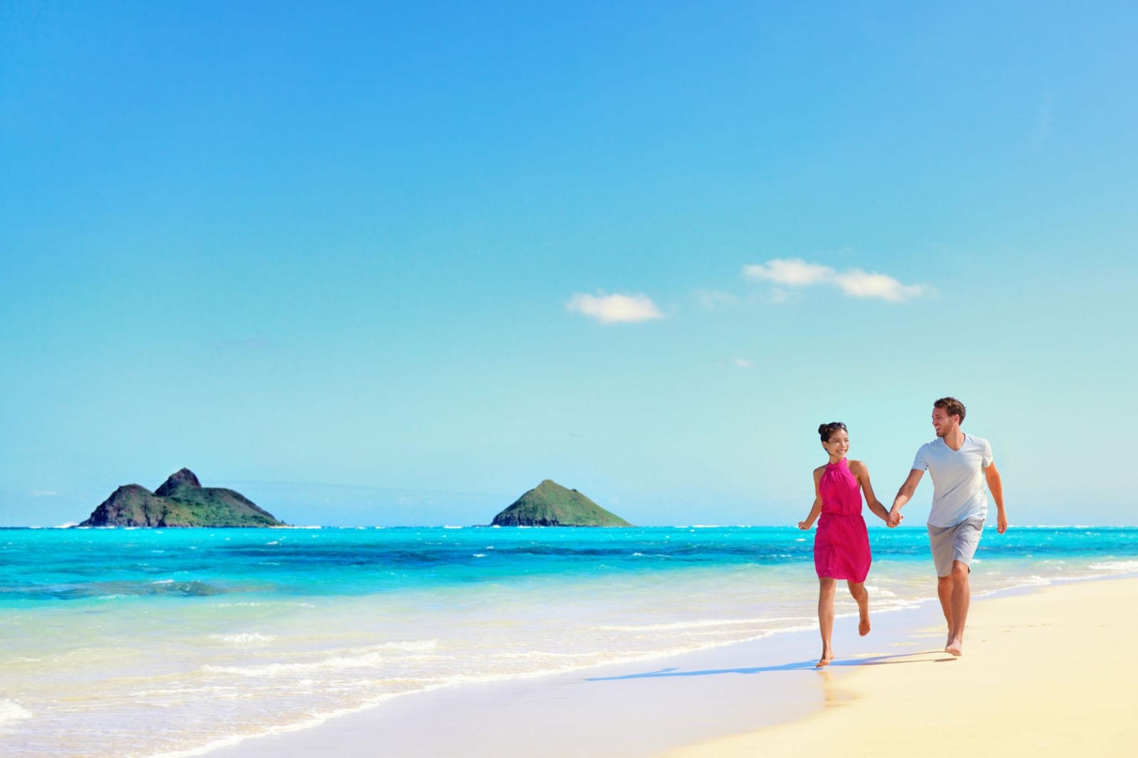 Couple holding hands and strolling on Lanikai Beach with the Mokulua Islands offshore — the kind of daily walking that powers recovery after joint replacement.