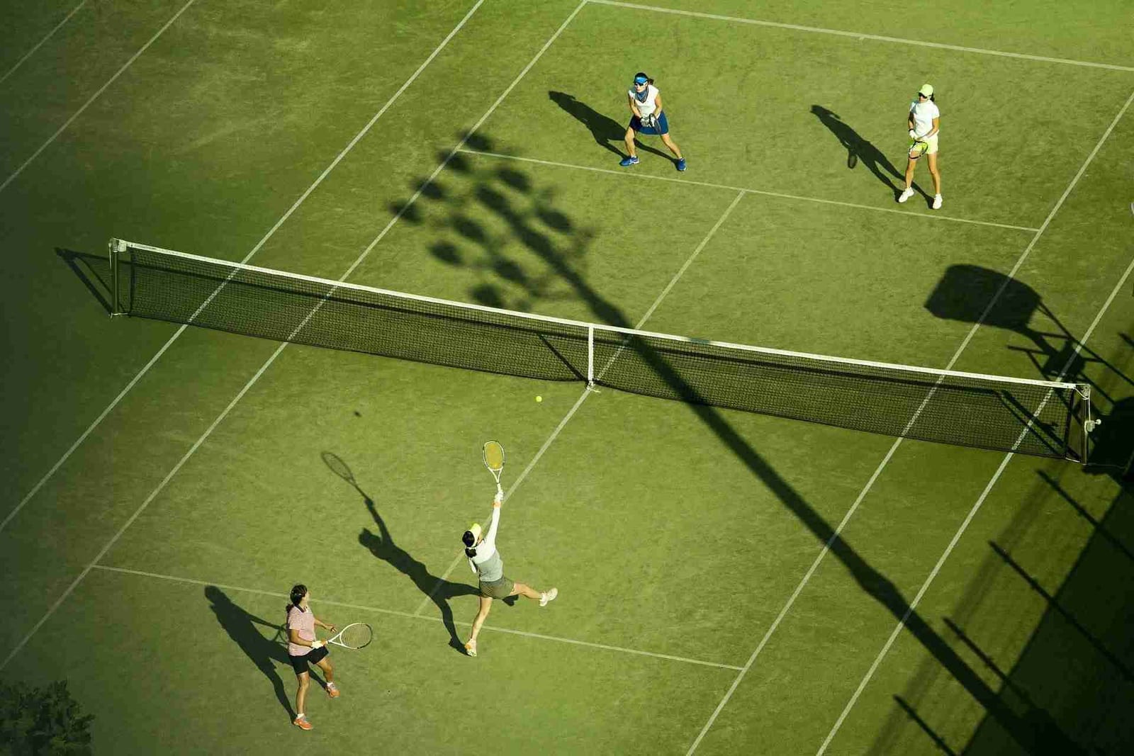 Aerial view of four players in a doubles match on a grass court, the kind of court sport many patients return to after joint replacement.