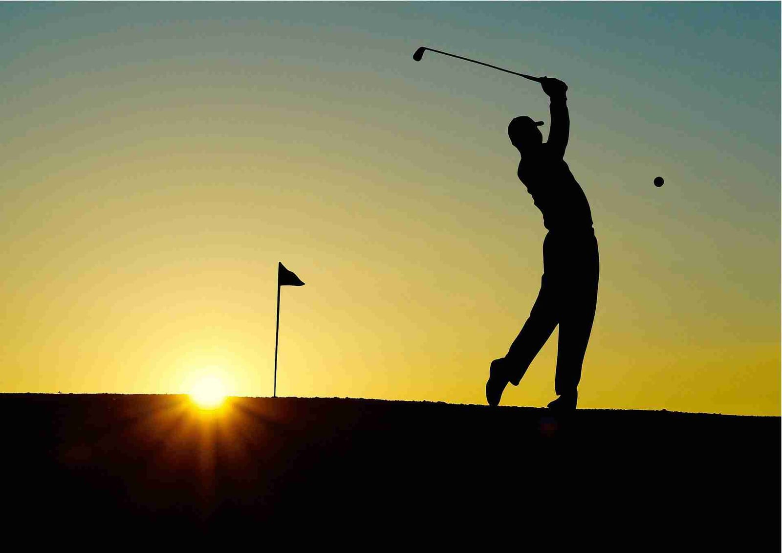 Silhouette of a golfer completing a full swing at sunset near the flagstick.