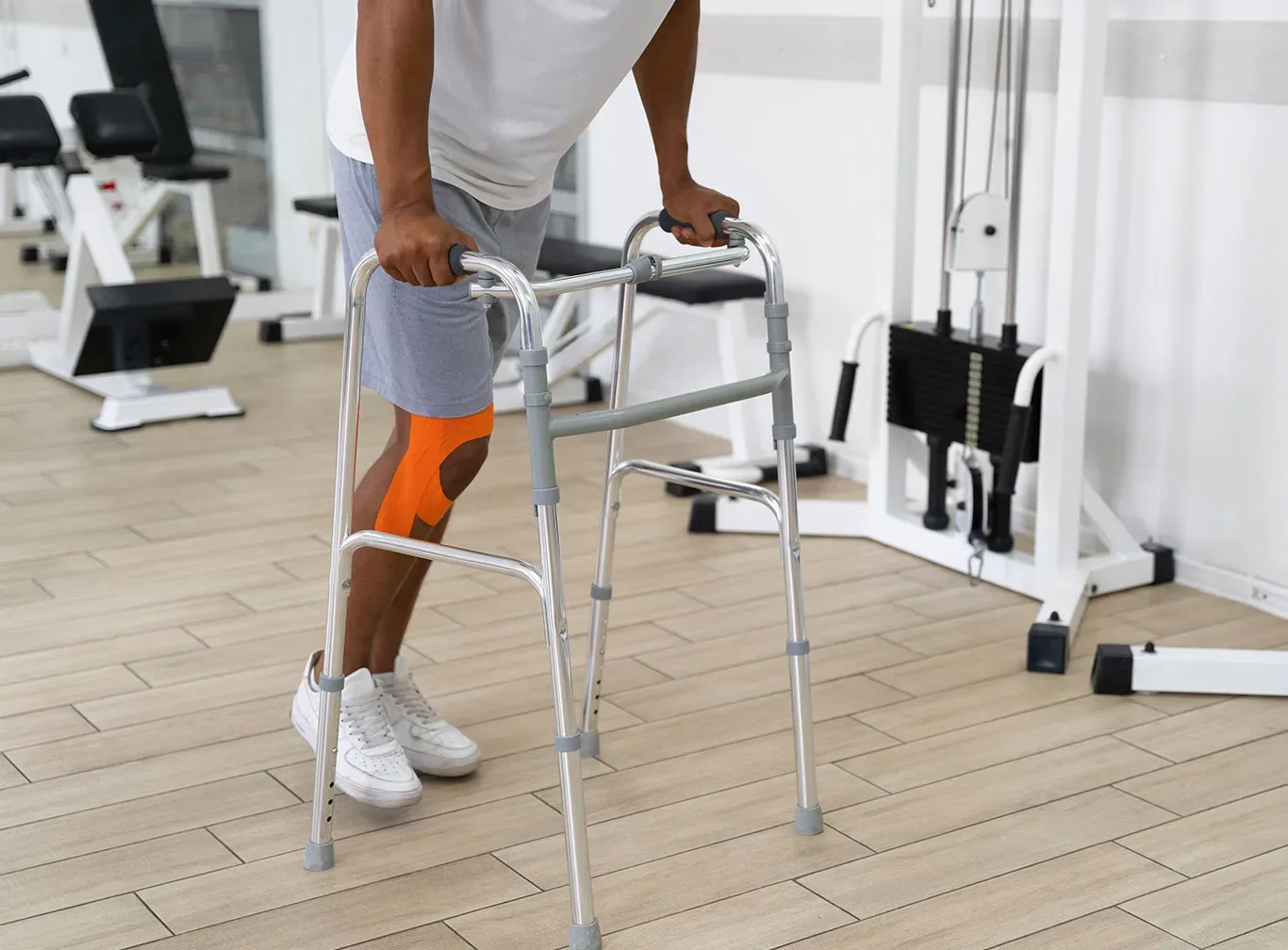 Patient with kinesiology tape on his knee walking with a walker in a physical therapy gym.
