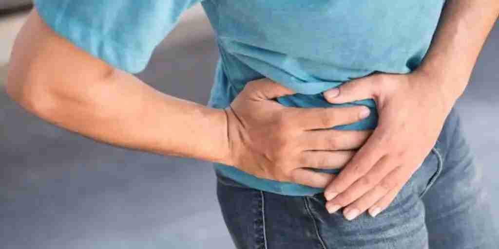 Man in a blue shirt pressing both hands against his painful hip.