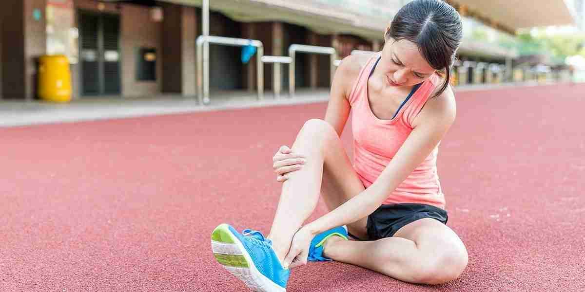 A young runner sits on a track holding her painful ankle after an injury.