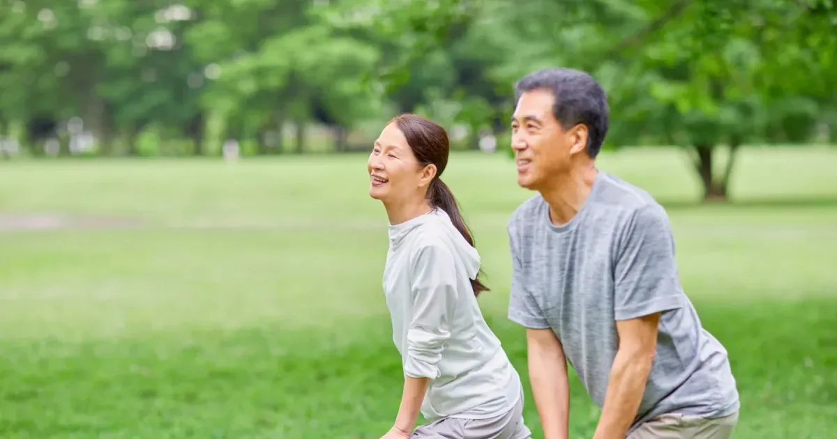 An older couple stretches together in a green park, staying active to ease knee arthritis.