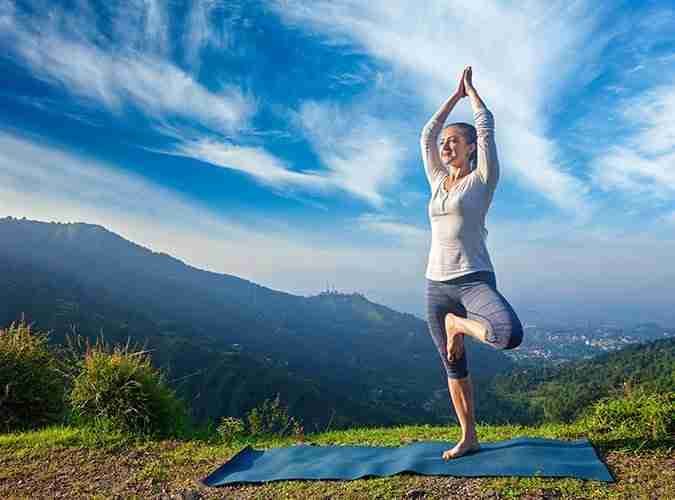 A woman balances in yoga tree pose on a mountain overlook, demonstrating joint-friendly exercise.