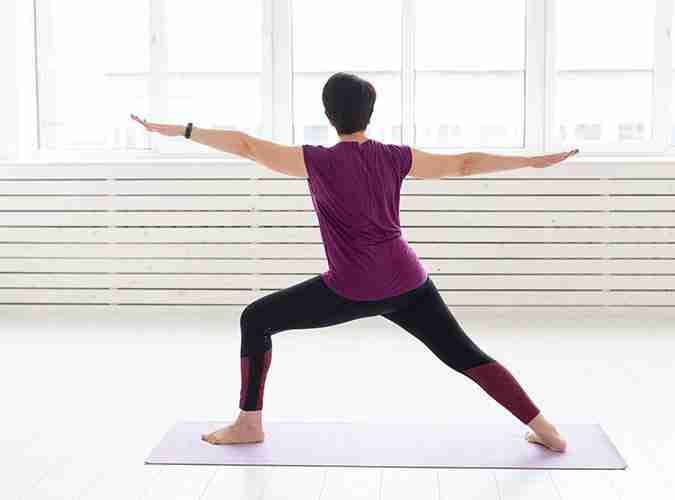 A woman practices the Warrior Two yoga pose, which builds the leg and knee strength that supports a new knee.
