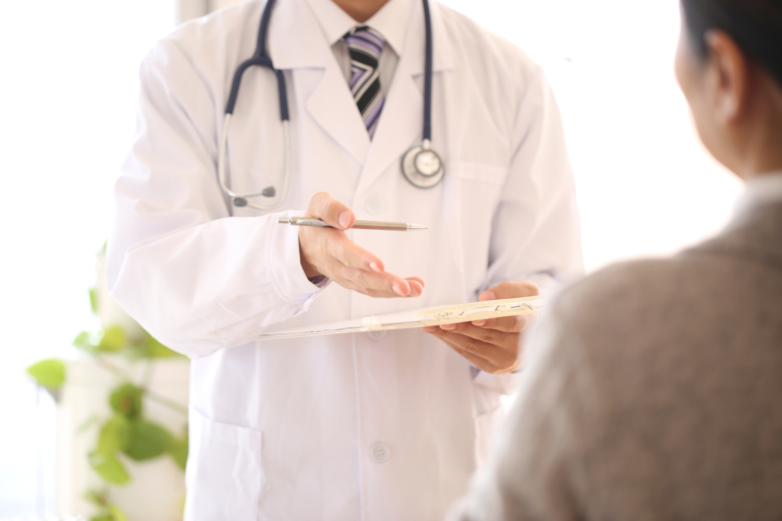 A physician with a clipboard walks a patient through insurance paperwork during an office visit.