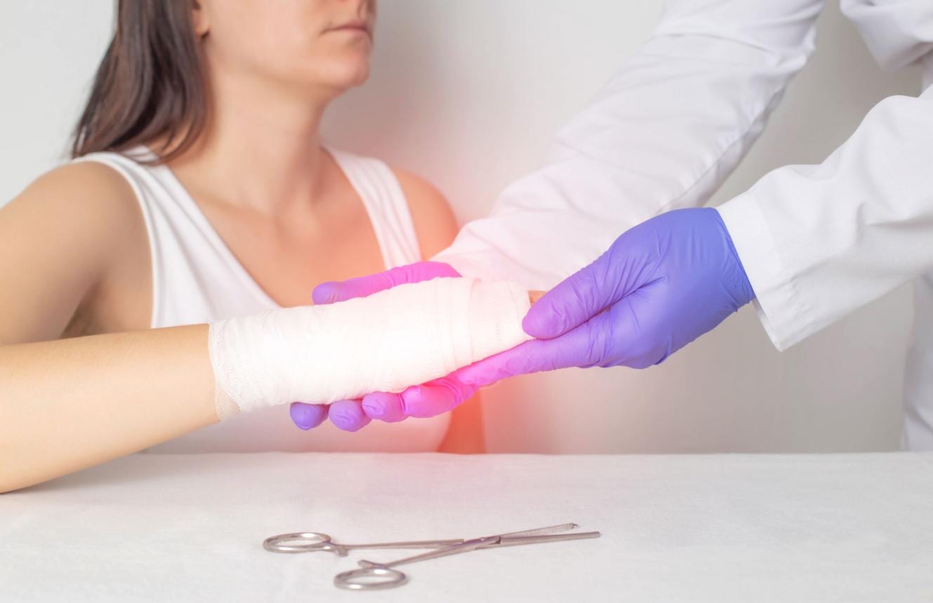 Doctor in gloves supporting a patient's bandaged wrist during an exam.
