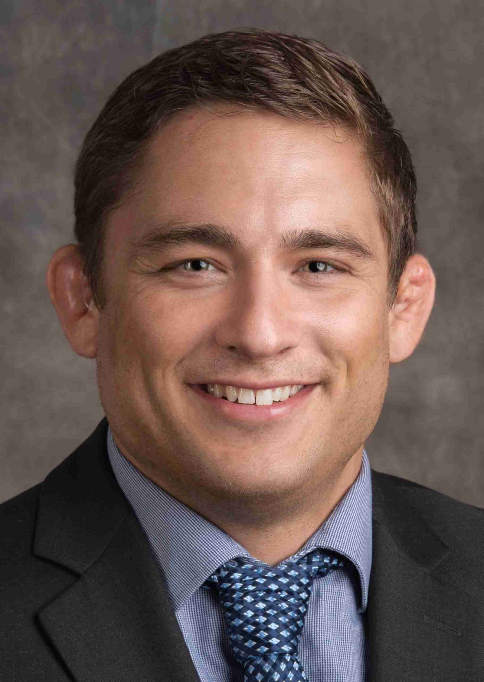 Dr. Paul Morton, fellowship-trained hip and knee replacement surgeon in Honolulu, in a formal studio headshot wearing a dark suit and blue tie.