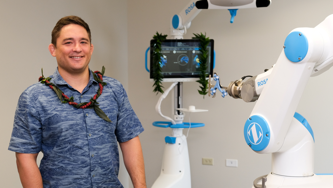 Dr. Paul Morton wearing a maile lei beside the ROSA robotic surgical system in Honolulu.