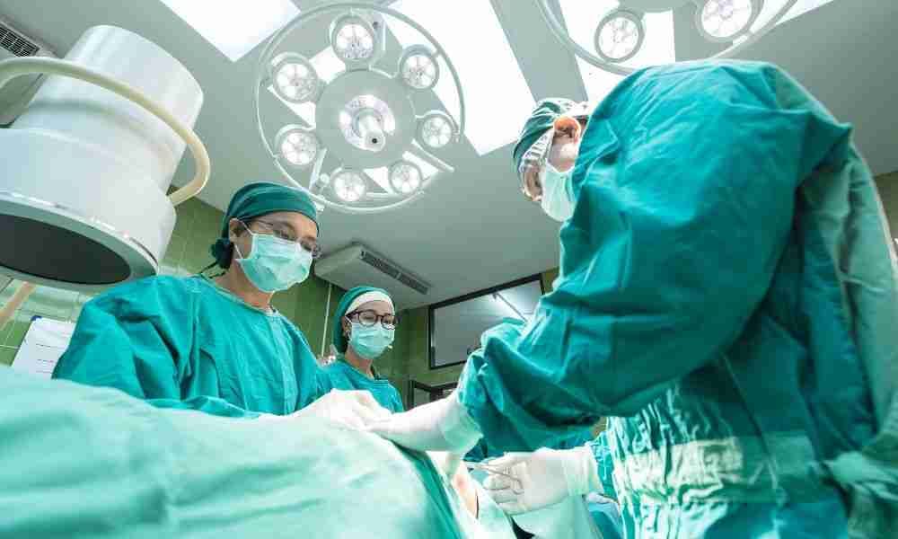 A surgical team in gowns and masks works beneath operating room lights during a procedure.