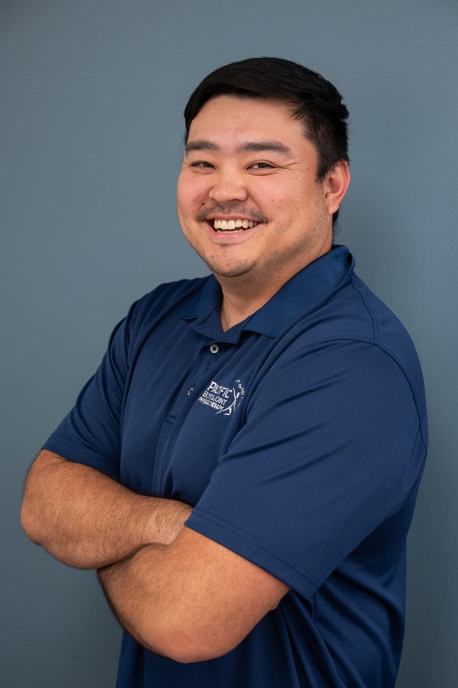 Bryson Naito of PB&J Physical Therapy smiling in a navy Pacific Bone & Joint polo.